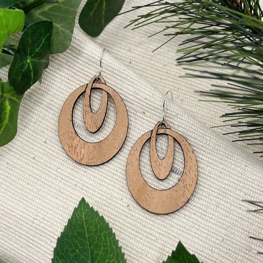 Wooden hoop earrings on a textured surface with green leaves in the background