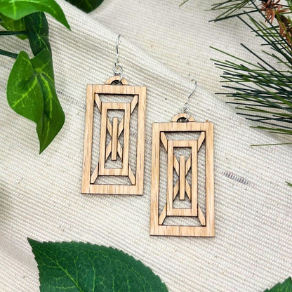 Rectangular geometric art deco earrings made of red oak and recycled sterling silver  on a textured surface with green leaves.
