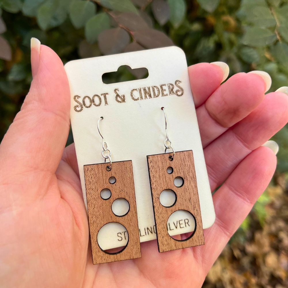 Wooden earrings on a 'Soot & Cinders' card held in a hand with a natural background.