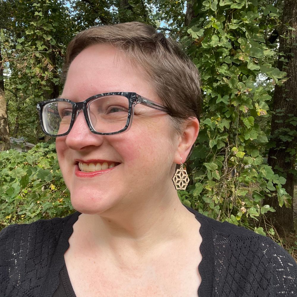 Person with glasses and earrings standing in front of green foliage wearing hexagonal wood and recycled sterling silver earrings 