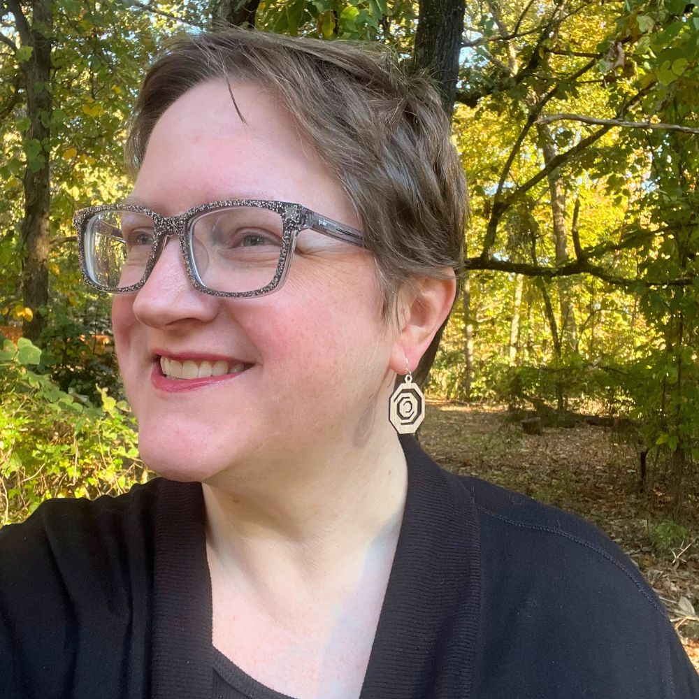 Woman with glasses and a black top standing in a forest wearing Octagonal red oak and recycled sterling silver earrings 