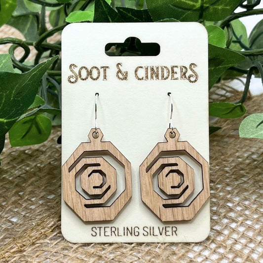 Octagonal geometric earrings made of solid red oak wood and recycled sterling silver on a 'Soot & Cinders' branded card with green leaves in the background