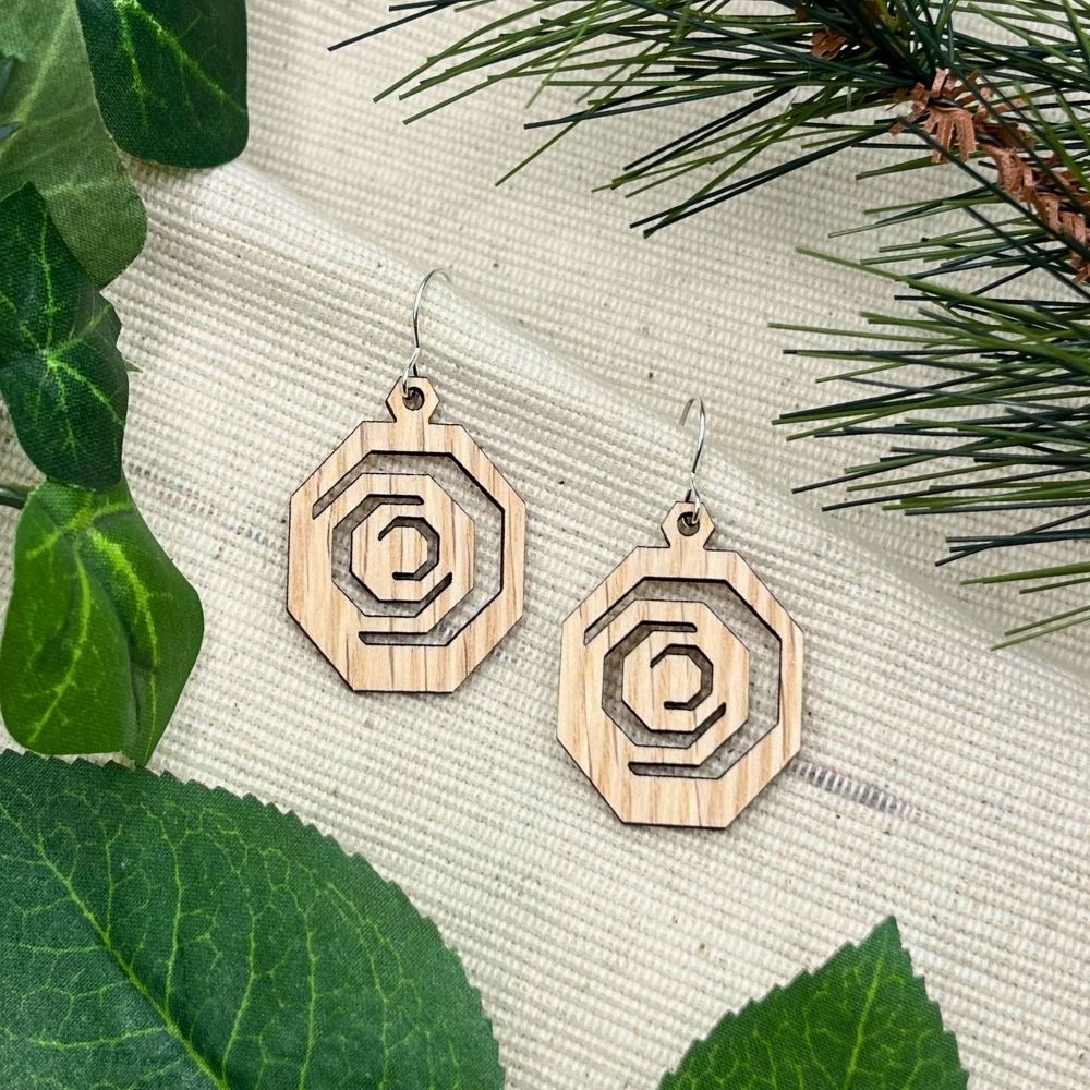 Wooden geometric earrings on a textured surface with green leaves and branches.