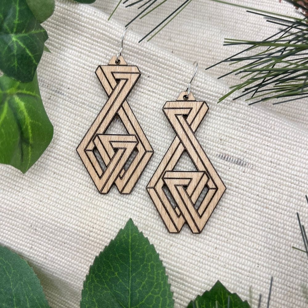 Wooden geometric earrings on a textured white surface with green leaves.