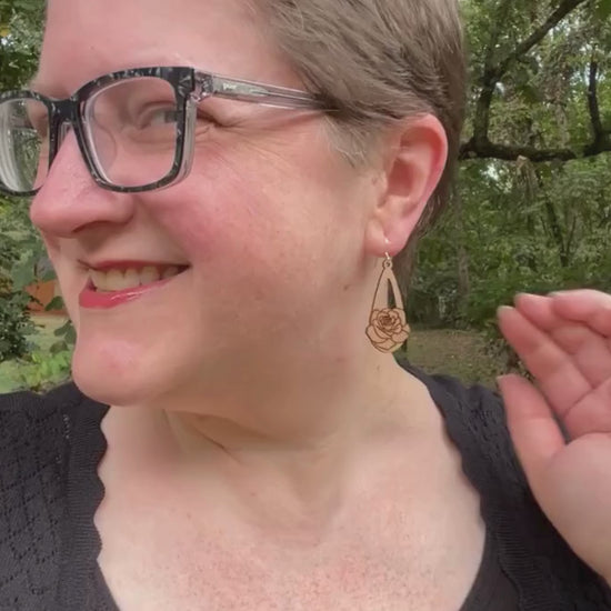 video showing a woman wearing wooden earrings engraved with roses, then a hand is shown holding the earrings while the earrings' sustainability traits are listed.