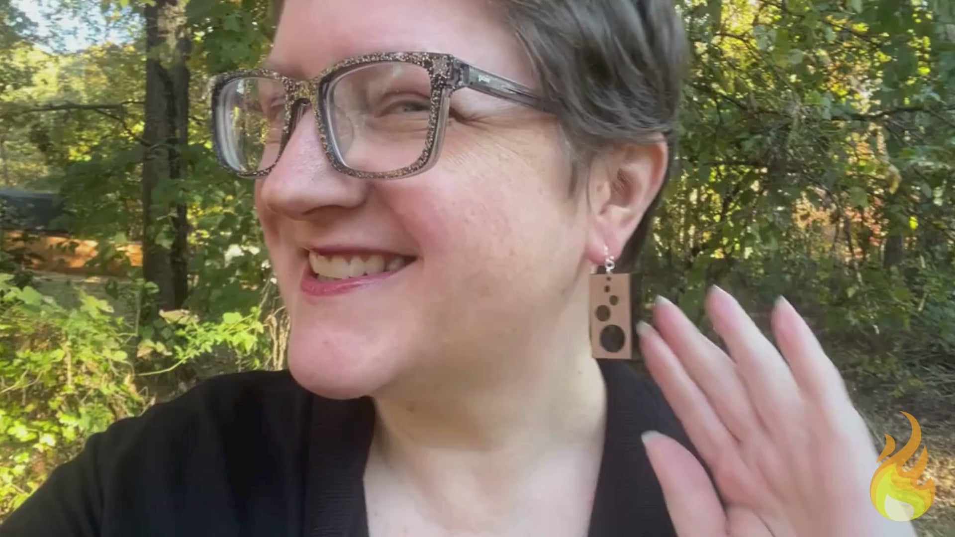 Video showing a woman modeling rectangular cherry wood and sterling silver earrings, then the earrings are shown lying in a woman's hand while text about the earrings' sustainability is seen. The video ends with the Soot & Cinders logo.
