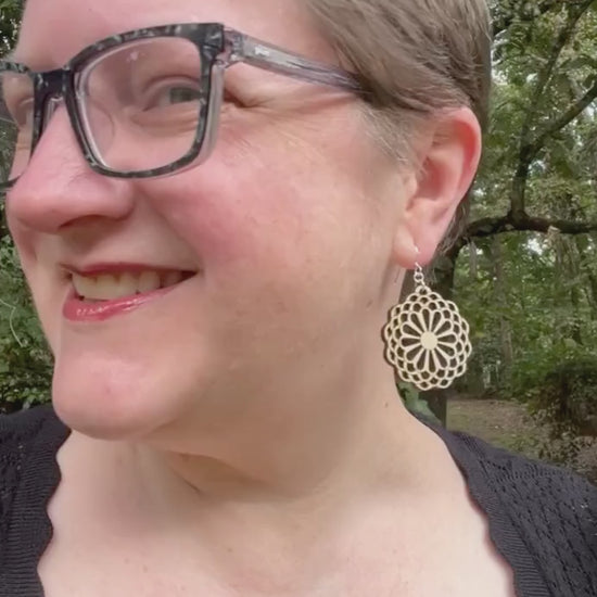 video of woman wearing statement earrings made of light colored wood and sterling silver in the style of large stylized flowers