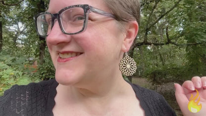video of woman wearing statement earrings made of light colored wood and sterling silver in the style of large stylized flowers