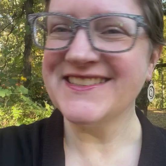 Video showing octagonal wooden red oak and sterling silver earrings being worn by a woman and then held in a hand on an earring card along with facts about its sustainability and that it is made in the USA.