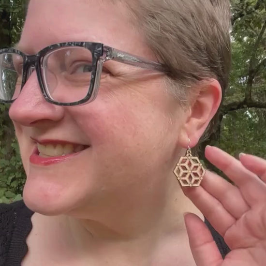 video showing a woman modeling hexagonal wood and silver earrings, then a hand is shown holding the earrings while the earrings' sustainability traits are listed