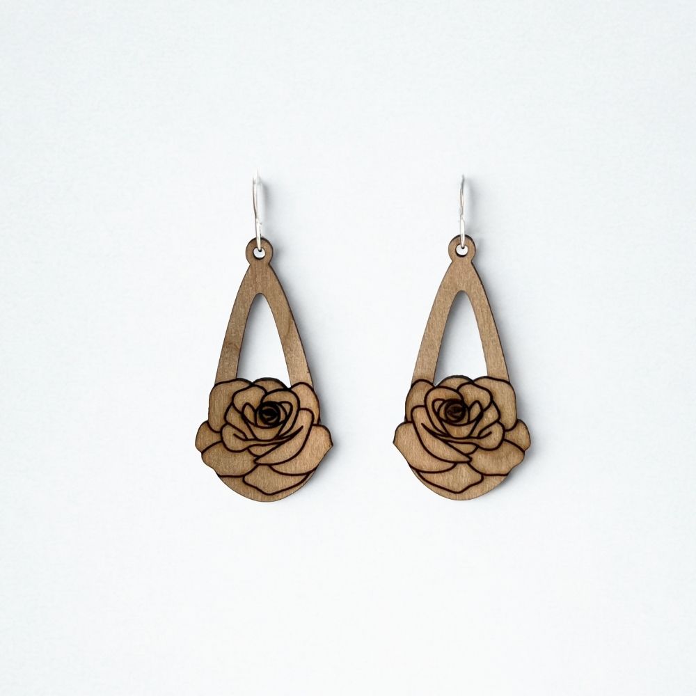 mahogany teardrop earrings with a rose engraved on them rest on a plain white background 