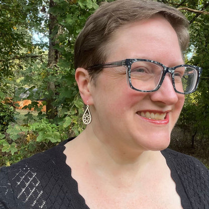 woman with a black cardigan wearing Sterling silver and white wood teardrop earrings with intricate snowflake-like designs in front of trees.