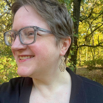 Person wearing glasses and a geometric earring in a forest setting