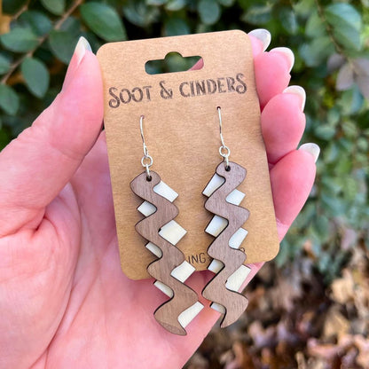 mahogany and aspen wood zigzag pattern earrings made with recycled sterling silver held in a hand in front of leaves