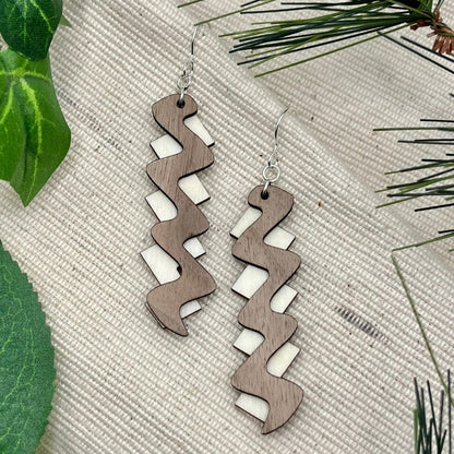 mahogany and aspen wood zigzag pattern earrings made with recycled sterling silver on a textured surface with green leaves.